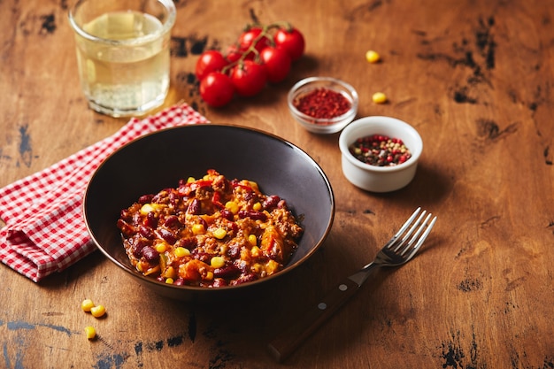 Chili con carne com feijão moído e milho em uma tigela escura sobre fundo de madeira mexicano e texas ...