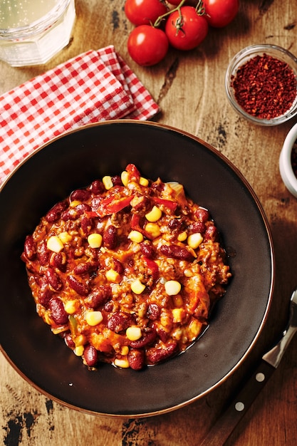 Chili con carne com feijão moído e milho em uma tigela escura sobre fundo de madeira mexicano e texas ...