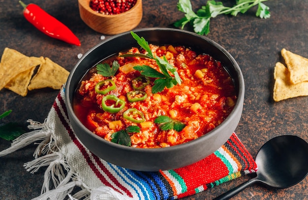 Chili con Carne in einer Schüssel mit Tortillachips auf dunklem Hintergrund. Selektiver Fokus der mexikanischen Küche