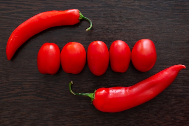 Chilischoten und Tomaten auf einem dunklen hölzernen Hintergrund