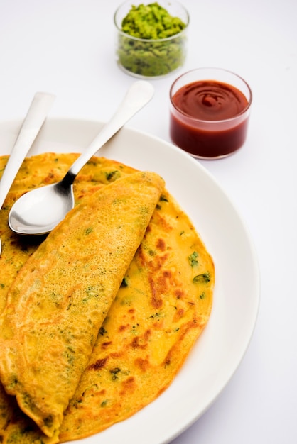 Foto chilla ou besan cheela é uma panqueca simples feita com farinha de grão de bico e alguns ingredientes básicos servida com chutney verde e molho de tomate, também conhecida como omelete vegetal