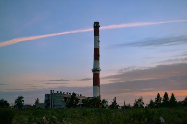 La chimenea alta de una caldera contra el telón de fondo de un hermoso cielo matutino y nubes