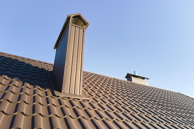 Chimenea en la azotea de la casa cubierta con tejas metálicas en construcción. Revestimiento de azulejos del edificio. Desarrollo inmobiliario