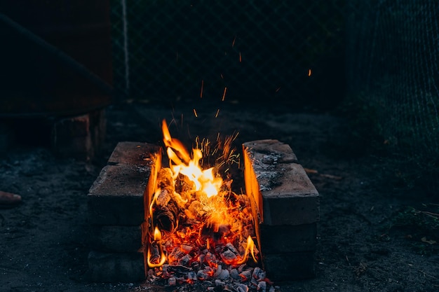 Chimenea para barbacoa en la naturaleza Chimenea al aire libre por la noche Hermoso fuego alto sobre fondo oscuro Chispas del fuego Ceniza del hogar