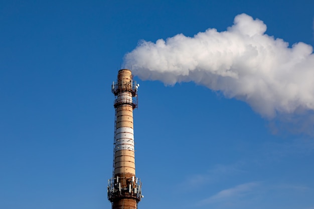 Chimenea de la fábrica que sopla el humo del tubo en el fondo del cielo azul durante el invierno. La contaminación del aire y el calentamiento global causado por la antigua planta de energía industrial