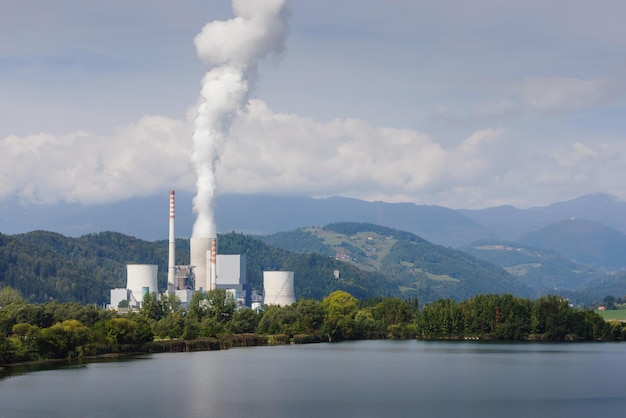 Chimenea humeante en la central térmica cerca del lago y la naturaleza verde