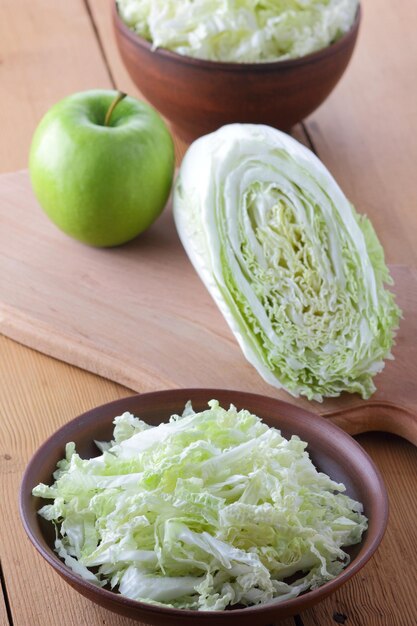 Chinakohl-Salat-Zubereitung in einer Tonschale Frischer Chinakohl und grüner Apfel auf einem hölzernen Hintergrund Closeup Bio-Lebensmittel