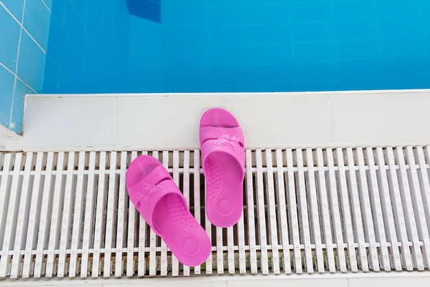 Chinelos cor de rosa ficam à beira da piscina com água azul em um dia ensolarado