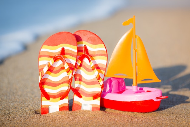 Chinelos e veleiro de brinquedo na praia