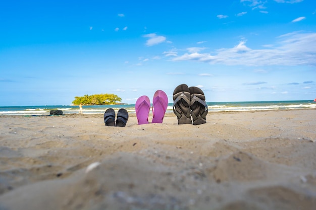 Chinelos ou sandálias no conceito de areia da praia de viagens em família de férias com sapatos de pai mãe e filho praia tropical no brasil com pessoa tirando fotos de si mesmo ao fundo