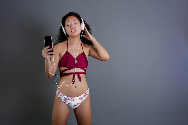 Chinês fofo e engraçado de biquíni ouvindo música no smartphone e fones de ouvido