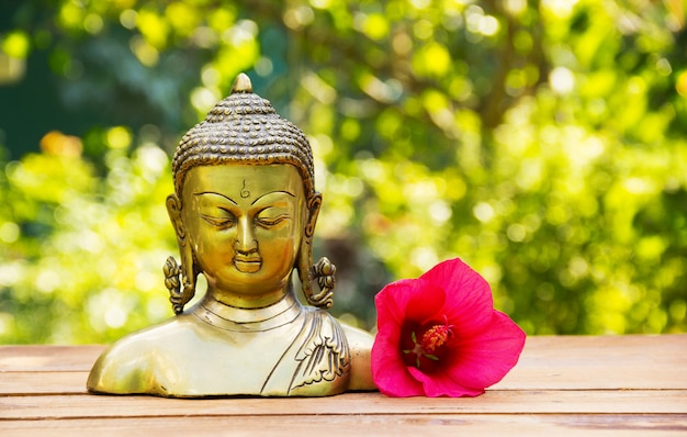 Chinesische Buddha-Skulptur und rosa Hibiskusblume auf grünem natürlichem Hintergrund