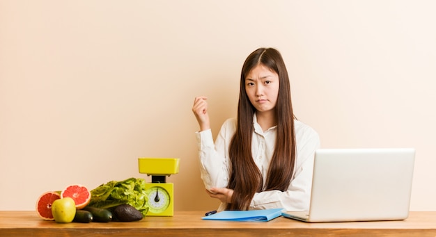 Chinesische Frau des jungen Ernährungswissenschaftlers, die mit ihrem Laptop berührt zurück vom Kopf arbeitet, eine Wahl denkt und trifft.