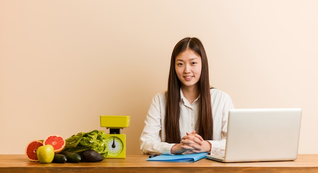 Chinesische Frau des jungen Ernährungswissenschaftlers, die mit ihrem Laptop glücklich, lächelnd und nett arbeitet.