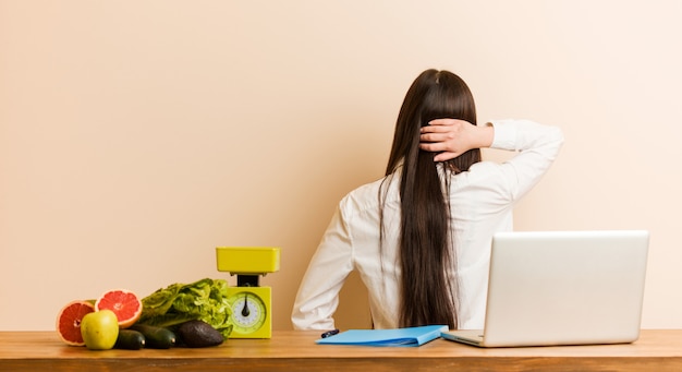 Chinesische Frau des jungen Ernährungswissenschaftlers, die mit ihrem Laptop von hinten denkt an etwas arbeitet.