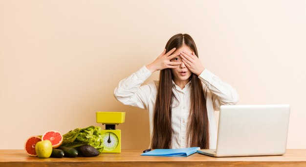 Chinesische Frau des jungen Ernährungswissenschaftlers, die mit ihrem Laptopblinken durch die Finger erschrocken und nervös arbeitet.