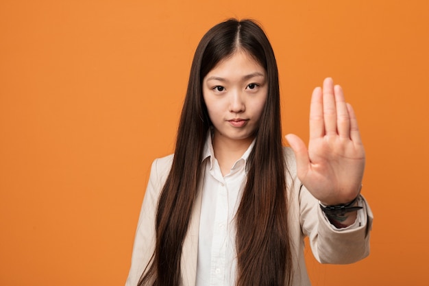 Chinesische junge Geschäftsfrau, die mit ausgestreckter Hand steht, die Stoppschild zeigt, das Sie verhindert.