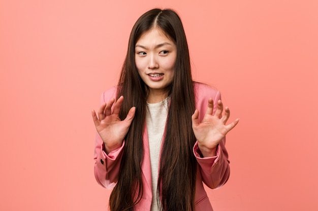Chinesische junge Geschäftsfrau, die rosa Anzug trägt und jemanden ablehnt, der eine Geste des Ekels zeigt.