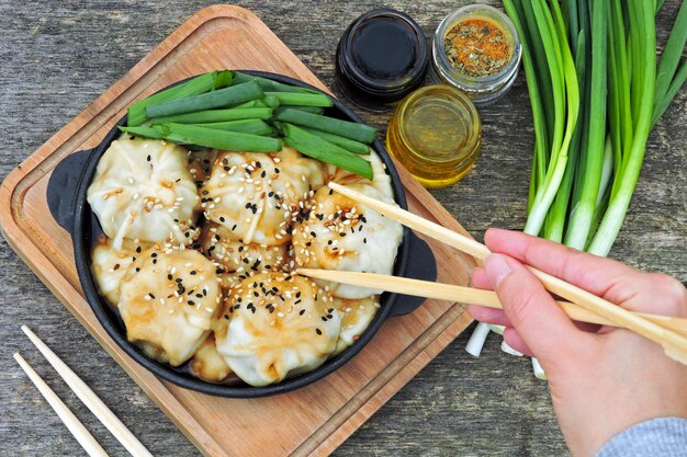 Chinesische Knödel mit Sojasauce, Frühlingszwiebeln und Sesam in einer gusseisernen Pfanne. Knödel im chinesischen Stil in einer Bratpfanne.