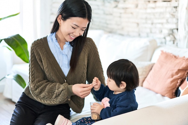 Chinesische Mutter füttert das Kleinkind mit Müsli auf dem Sofa