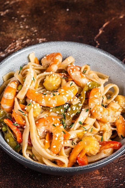 Chinesischer Wok Udon-Meeresfrüchte-Nudeln mit Garnelen in einer Schüssel anbraten. Schwarzer Hintergrund. Ansicht von oben.