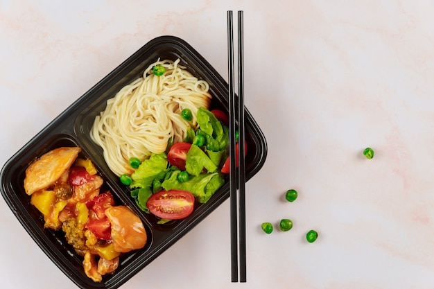 Chinesisches Essen im Plastikbehälter mit Essstäbchen. Konzept der Lebensmittellieferung.