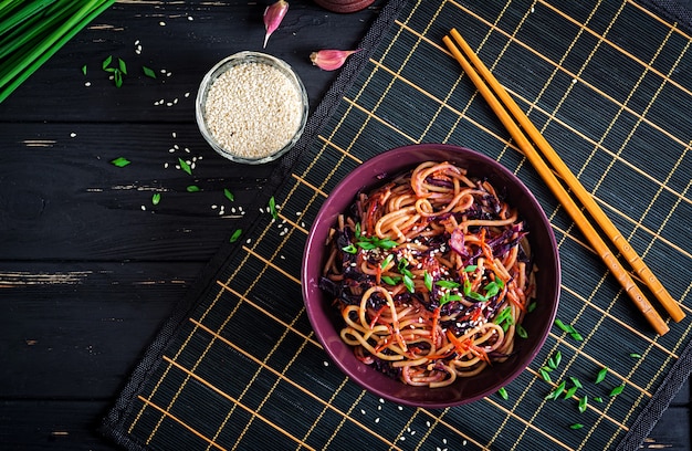 Foto chinesisches essen. stirfischrogennudeln des strengen vegetariers mit rotkohl und karotte in einer schüssel auf einem schwarzen hölzernen hintergrund. asiatische küche mahlzeit. ansicht von oben