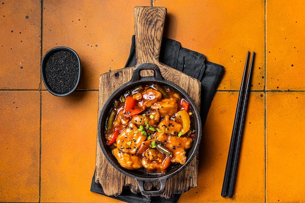 Chinesisches süß-saures Hähnchen mit bunter Paprika in einer Pfanne Orangefarbener Hintergrund Draufsicht