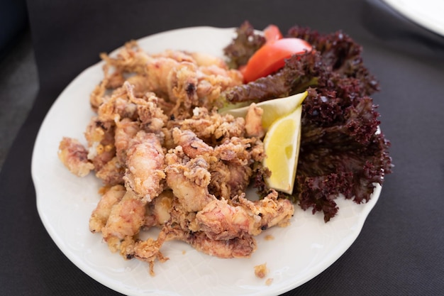 Foto chipirones fritos en un plato con lechuga limón y tomate tapa tradicional española de marisco