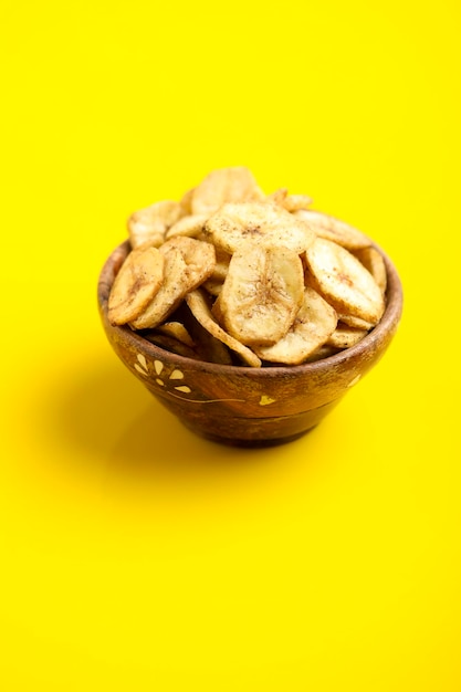 Chips de banana em uma tigela de madeira em fundo amarelo