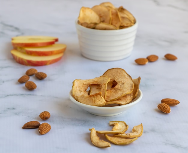 Chips de maçã em um prato branco perto das amêndoas em mármore