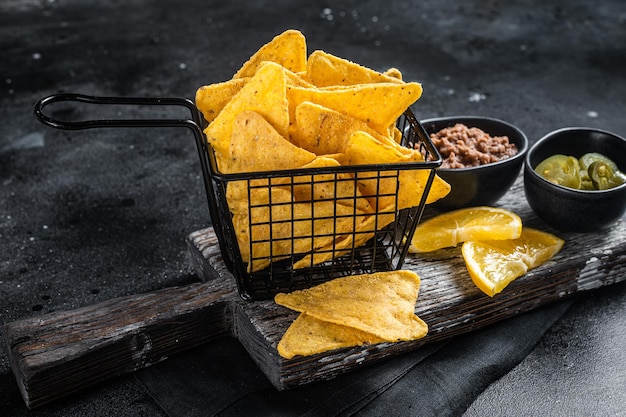 Chips de milho mexicanos nachos com Chili con carne e jalapeno em uma cesta Fundo preto Vista superior
