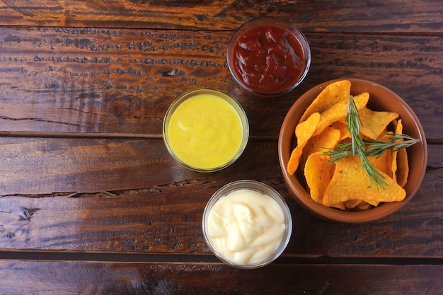 Foto chips de maíz nachos colocados en un recipiente de cerámica en una mesa de madera junto a salsas variadas