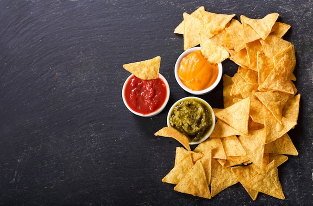 Chips de maíz de nachos mexicanos con guacamole, salsa y salsa de queso en la oscuridad