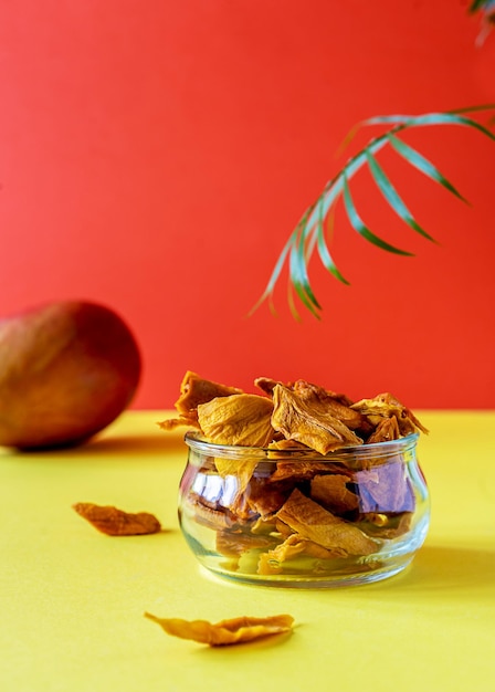 Chips de mango en un frasco de vidrio sobre fondo amarillo y naranja