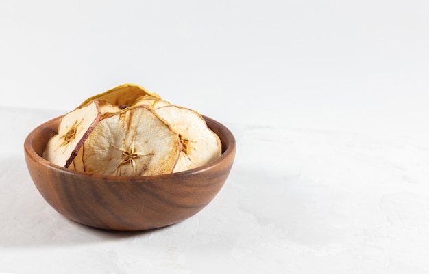 Chips de manzana seca en un recipiente de madera sobre un fondo de hormigón blanco.