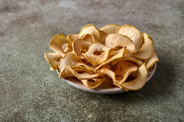 Chips de manzanas deshidratadas en la placa sobre fondo de madera con textura de cerca