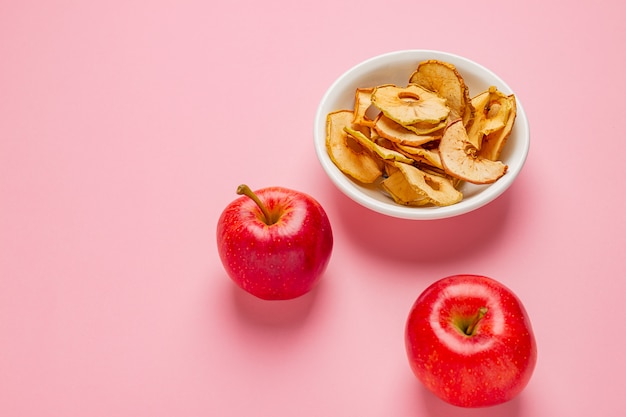 Chips de manzanas secas en un tazón de cerámica con manzanas rojas frescas en la mesa