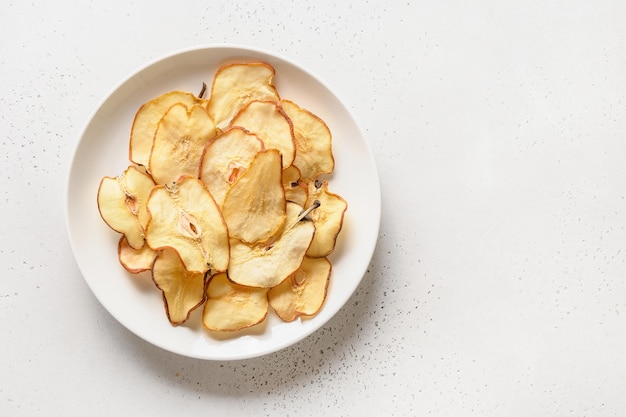 Chips de pera de frutas y agua en una sombra dura y soleada sobre un fondo de baldosas blancas Postre vegano sin azúcar Vista desde arriba Copiar espacio