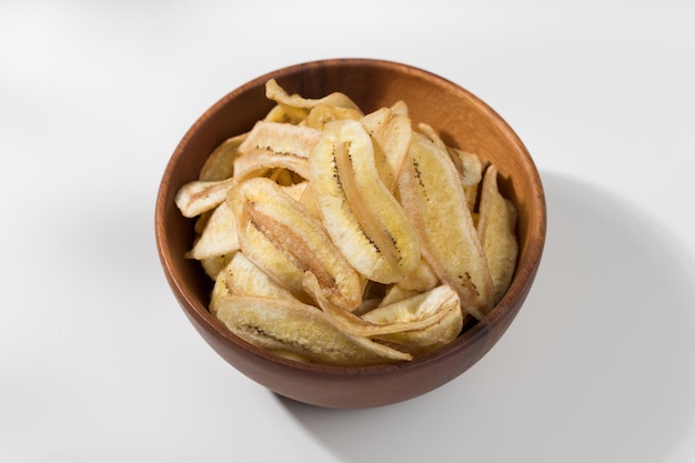 Chips de plátano en un cuenco de madera en una mesa blanca