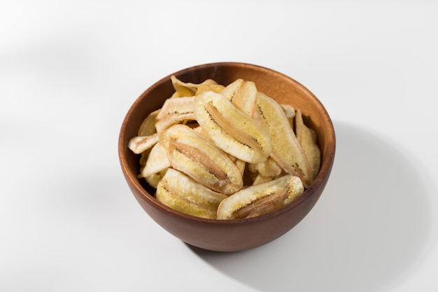 Chips de plátano en un cuenco de madera en una mesa blanca