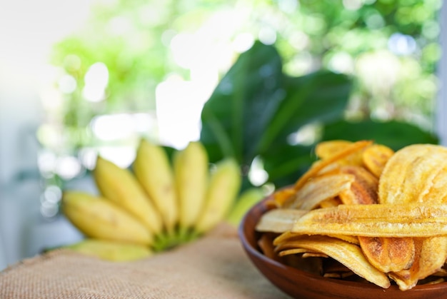 Foto chips de plátano en un recipiente contra el fondo de plátano joven cultivado