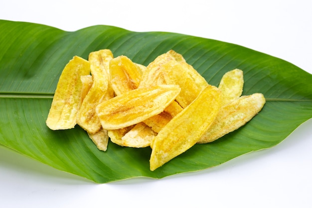 Chips de rebanada de plátano en hojas verdes sobre fondo blanco.