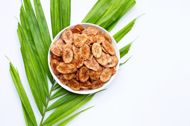 Chips de rodajas de plátano con hojas verdes sobre superficie blanca