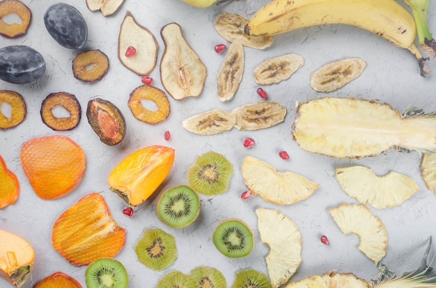 Chips secos variados e frutas maduras em fundo cinza. chips de frutas. conceito de alimentação saudável,