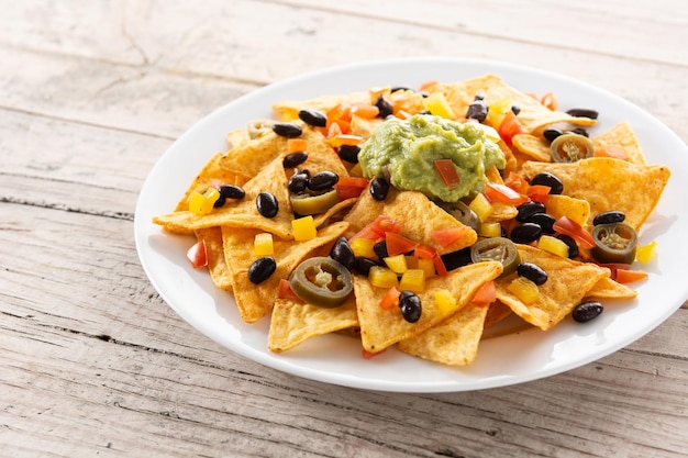 Chips de tortilla de nachos mexicanos con frijoles negros, guacamole, tomate y jalapeño sobre mesa de madera