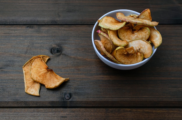 Chips von Äpfeln mit Zimt sind auf einer weißen Platte auf einer Tabelle von schwarzen hölzernen Brettern. Bio-Apfelchips. Getrocknete Früchte. Gesunder süßer Snack.