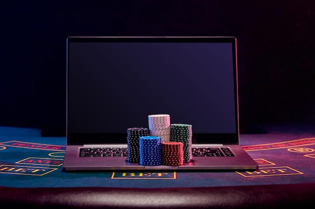 Chipshaufen befinden sich auf einem Laptop, der auf einer blauen Abdeckung des Spieltischs mit schwarzem Hintergrund steht