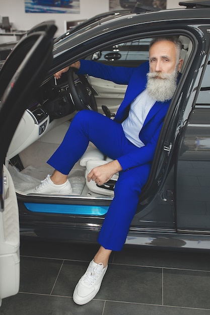 Foto chiqueiro velho em pé perto do automóvel de luxo. macho rico maduro no terno ao ar livre perto do carro.