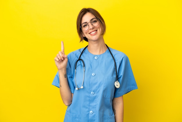 Chirurg Arzt Frau isoliert auf gelber Wand zeigt und hebt einen Finger im Zeichen des Besten lifting